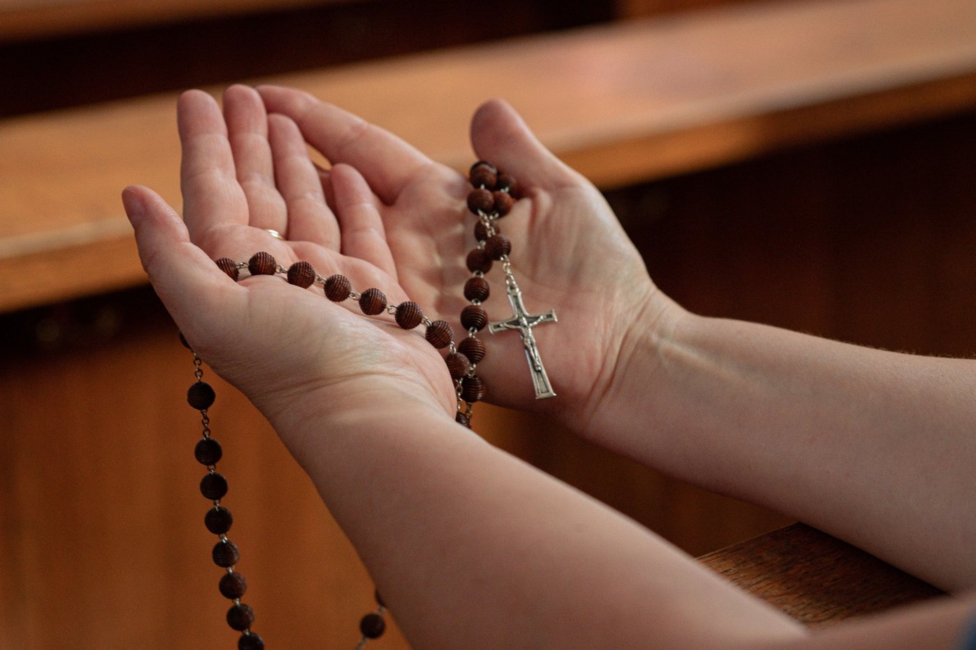 Mãos abertas segurando um terço, sinal de oração e confiança.